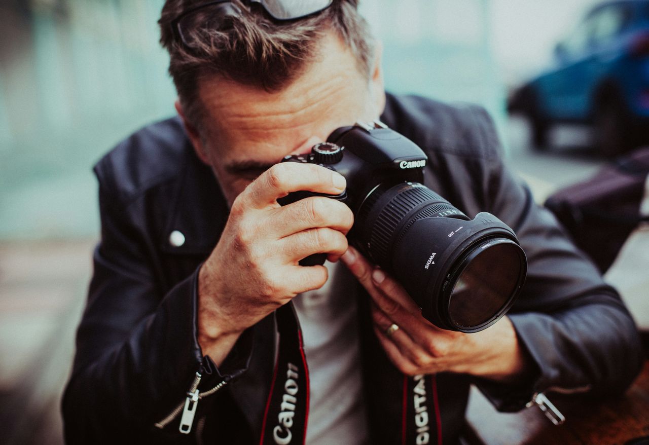Primer plano de un fotógrafo disparando con una cámara Canon en exteriores, comprometido con su trabajo, que ilustra el oficio sostenido en el tiempo