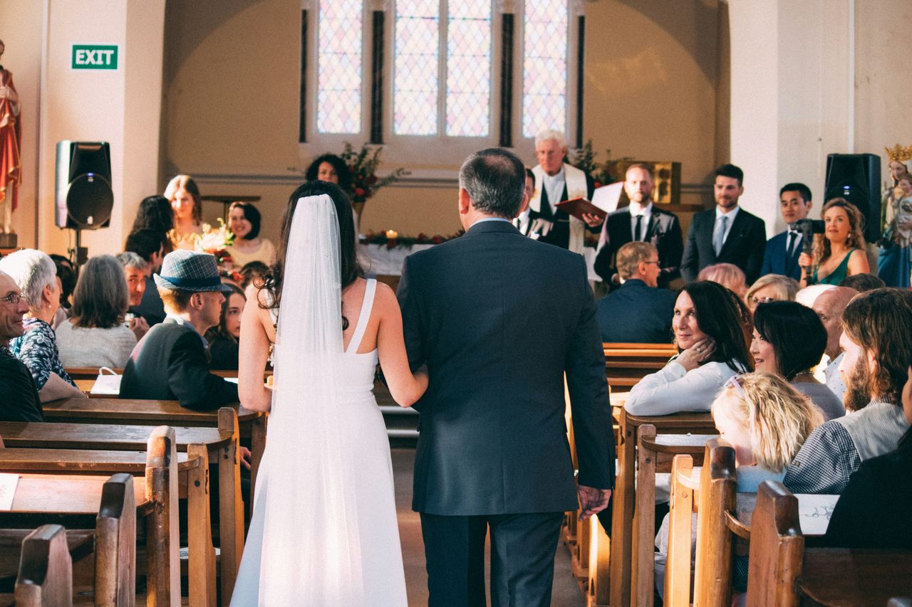 Novia caminando del brazo de su padre por el pasillo de una iglesia hacia el altar durante ceremonia de casamiento
