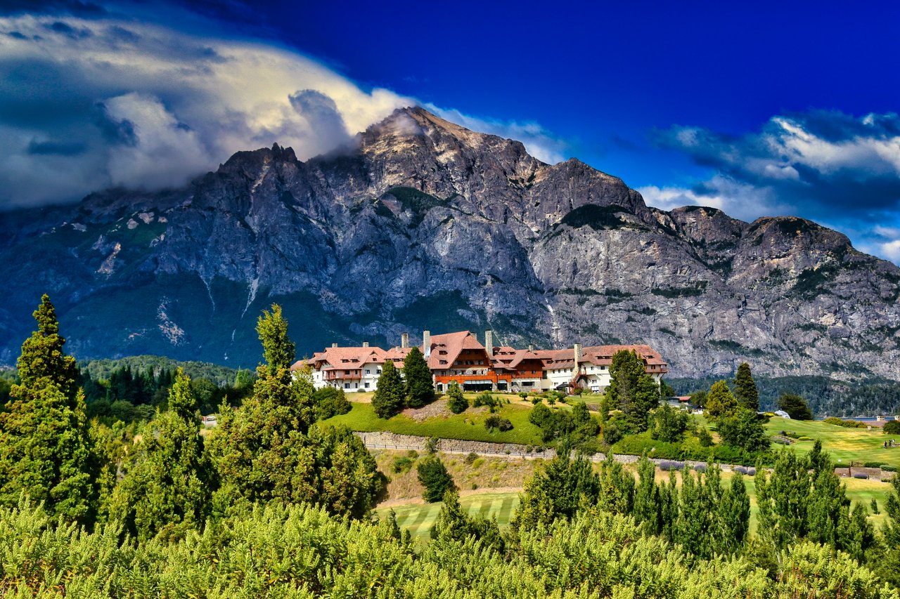 Hotel Llao Llao en plano elevado con la imponente cordillera patagónica y cielo dramático con nubes oscuras al fondo, una de las locaciones más icónicas de Bariloche para fotografía