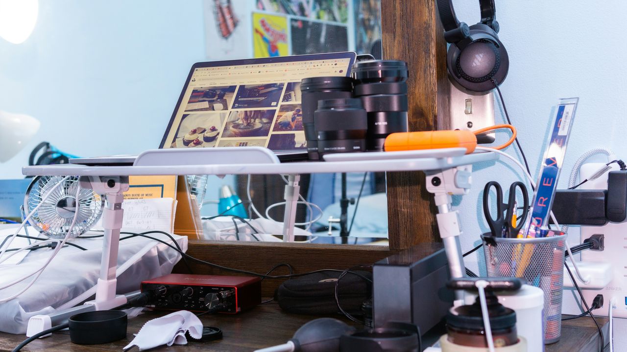 Escritorio de fotógrafo con una laptop mostrando una galería de Instagram en miniaturas, lentes apilados y auriculares, que representa la obsesión con las métricas de redes sociales