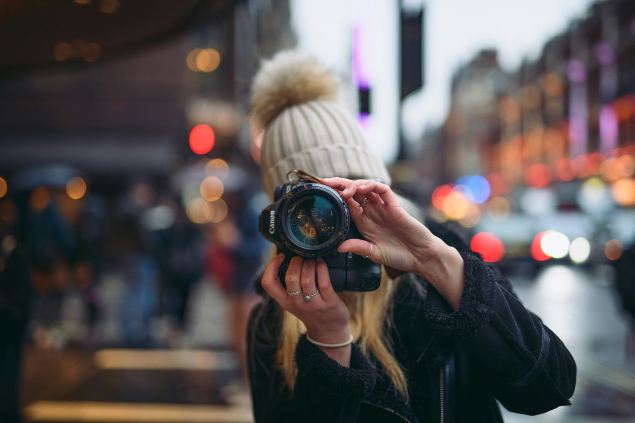 Fotógrafa de espaldas sacando foto a pareja de novios bailando en parque verde durante sesión de fotos