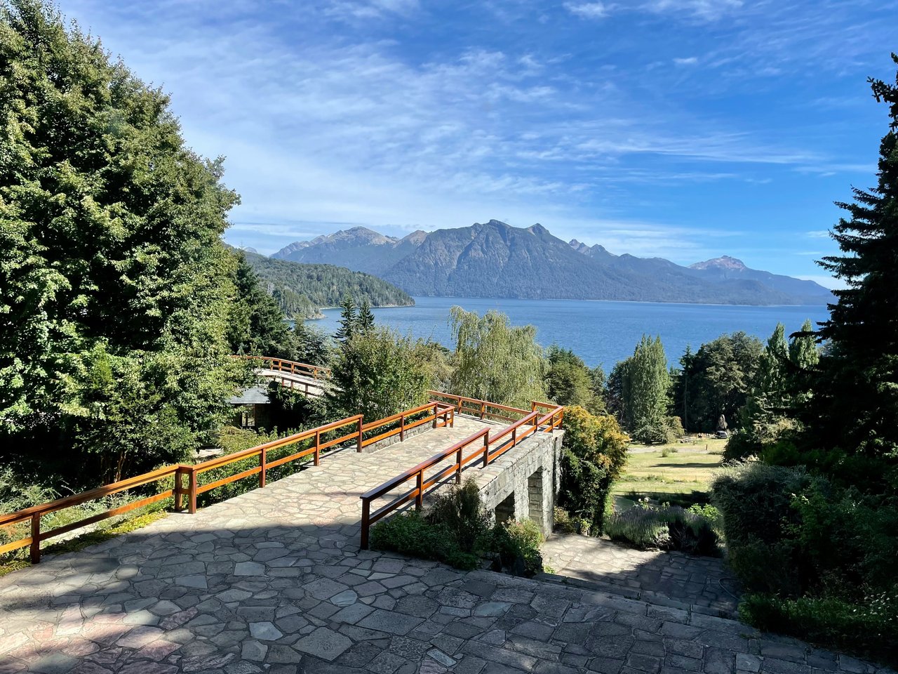 Pasarela de madera con barandas naranjas en mirador del Cerro Campanario con vista al Nahuel Huapi y montañas patagónicas de fondo, día soleado
