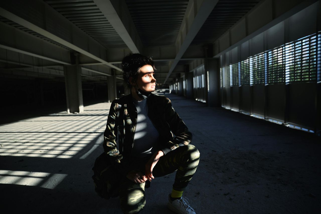 Persona agachada con sombras geométricas de persiana proyectadas por sol duro sobre el cuerpo y el piso, ejemplo de fotografía fine art con luz dura
