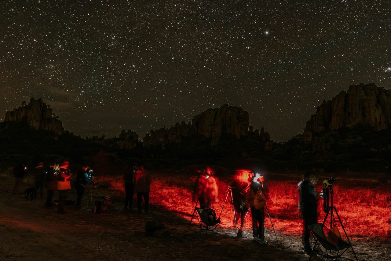 Grupo de fotógrafos con trípodes trabajando de noche en un valle de formaciones rocosas bajo un cielo estrellado, iluminados solo con luz roja para no perder la visión nocturna