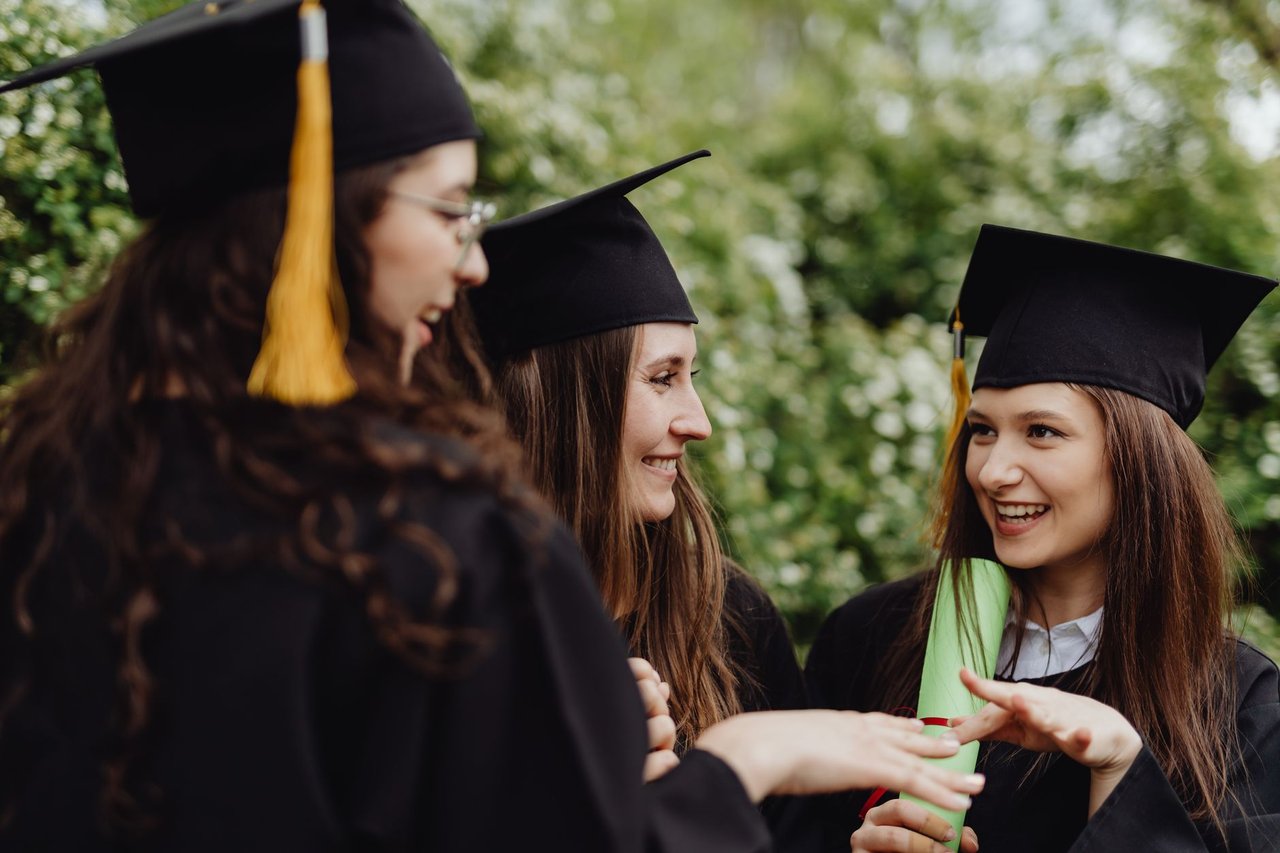 Tres egresadas con birrete y toga sonriendo al aire libre con el diploma en la mano, la sesión de egresados es el trabajo mejor pago del año escolar