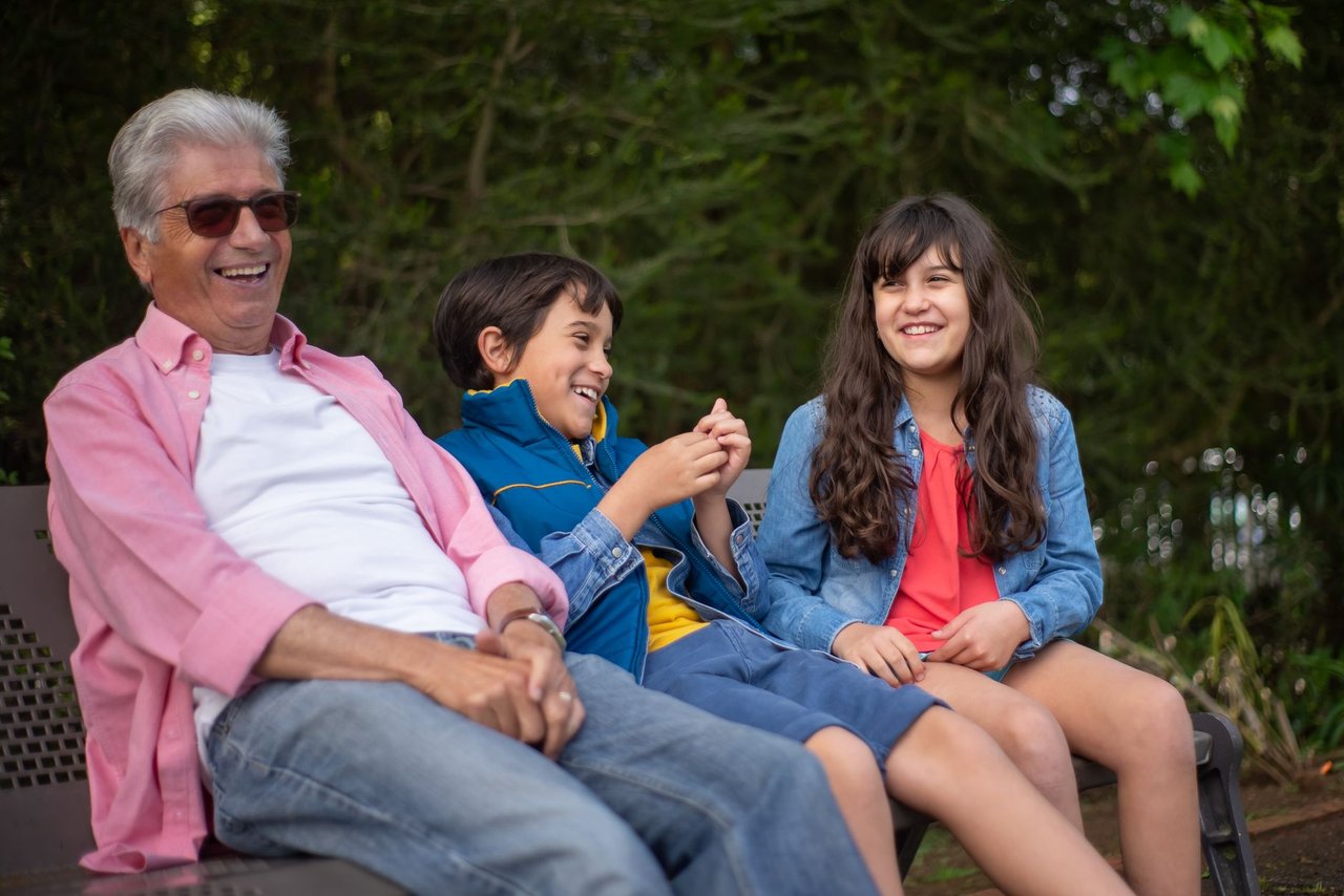 Abuelo sentado en un banco al aire libre junto a sus dos nietos durante una sesión de fotos familiar