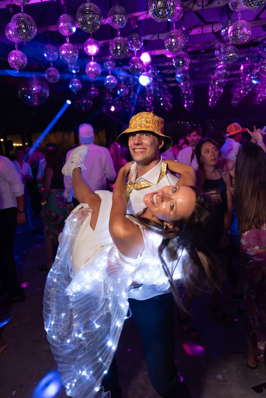 Pareja de jóvenes bailando y riendo en el carnaval carioca de una fiesta nocturna bajo bolas de espejo, el momento de más movimiento y menos luz de la noche
