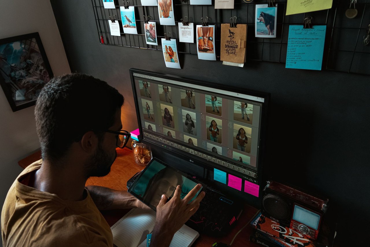 Fotógrafo trabajando frente a un monitor con una galería de fotos en una oficina en casa decorada con copias impresas colgadas en la pared