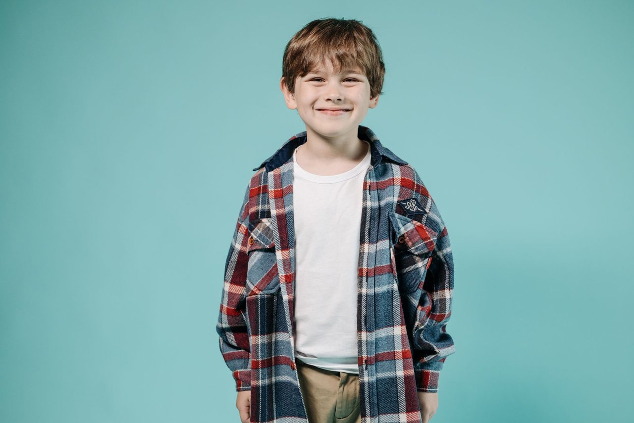 Retrato de estudio de un nene con camisa a cuadros sobre fondo celeste liso con luz pareja, el encuadre fijo que se repite en todas las individuales