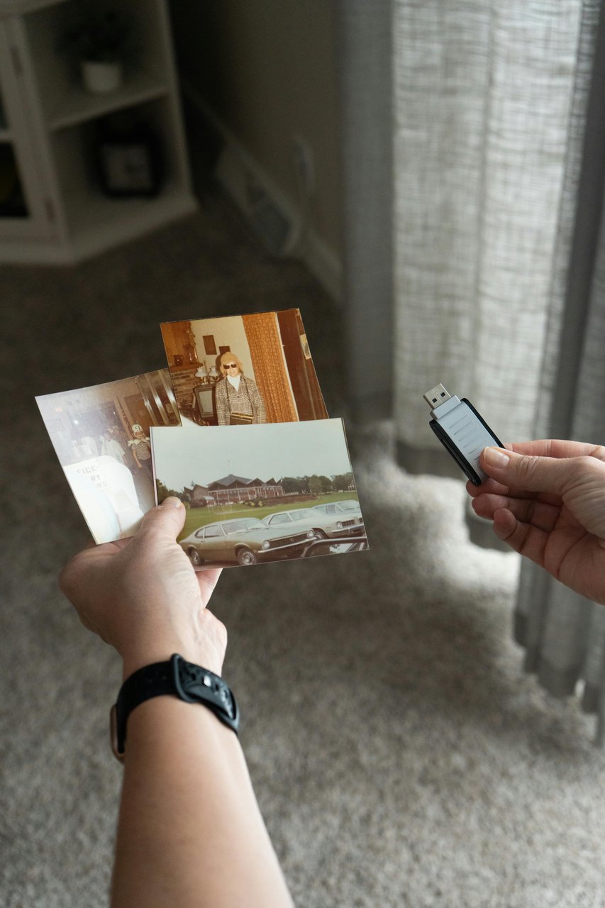 Manos sosteniendo tres copias impresas y un pendrive, la combinación de entrega física y digital de un trabajo fotográfico