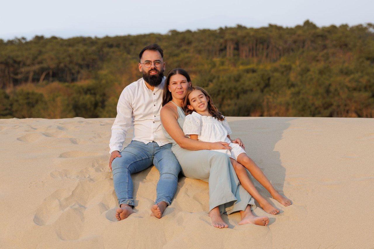 Familia de tres sentada sobre una duna de arena al atardecer durante una sesión de fotos familiar en exteriores