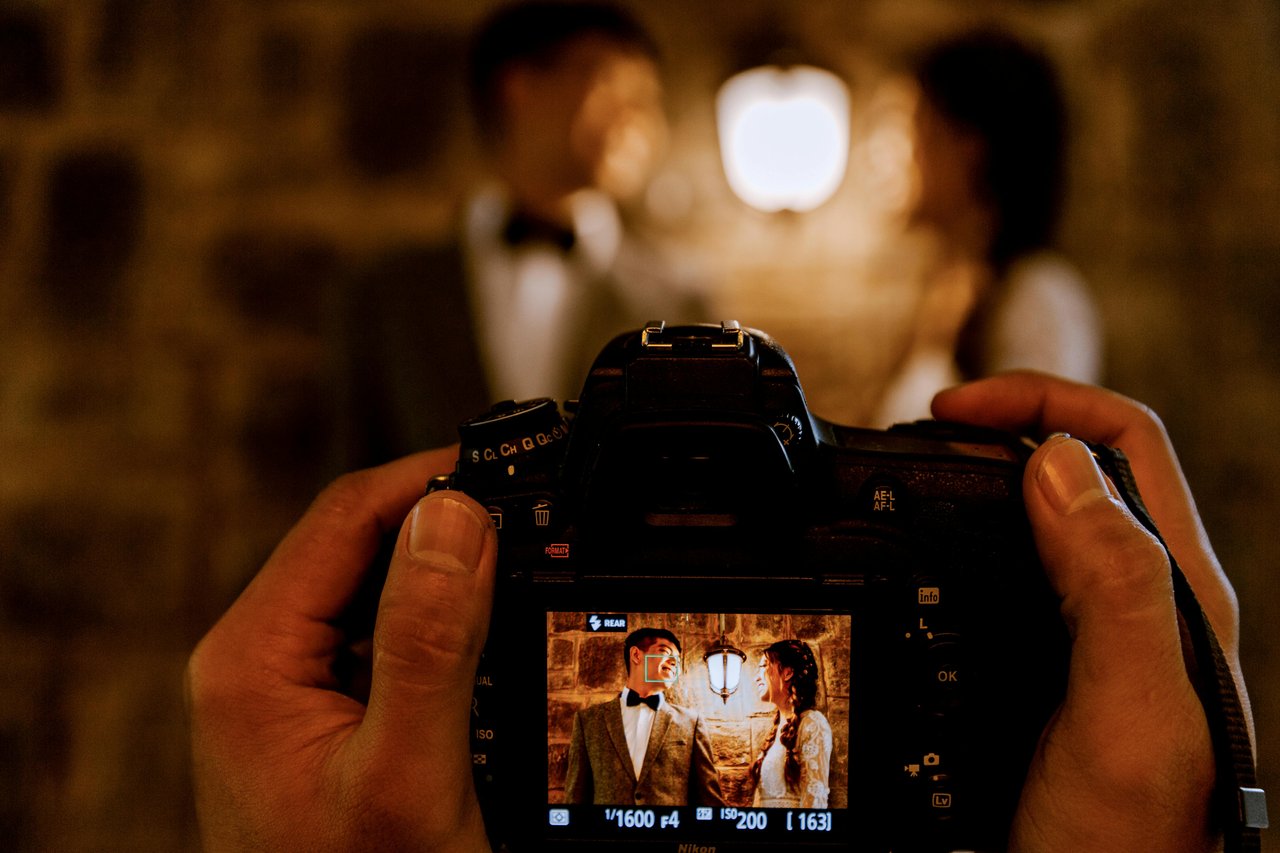 Vista de la pantalla trasera de una cámara Nikon mostrando una foto de los novios junto a un farol vintage durante la fiesta nocturna, ejemplo de cobertura de casamiento con poca luz