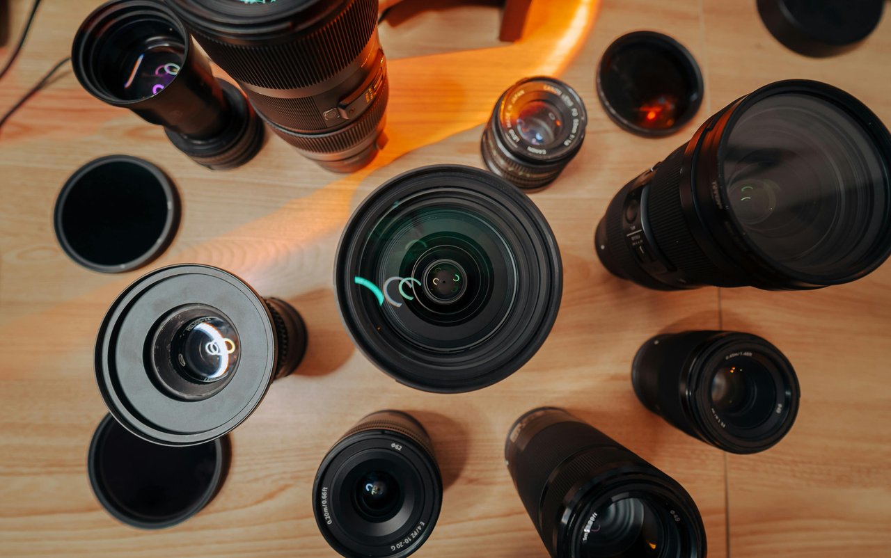 Varios lentes Sony y Canon de distintos tamaños junto a filtros dispuestos sobre una mesa de madera con luz cálida, que muestra el ecosistema de lentes detrás de cada montura