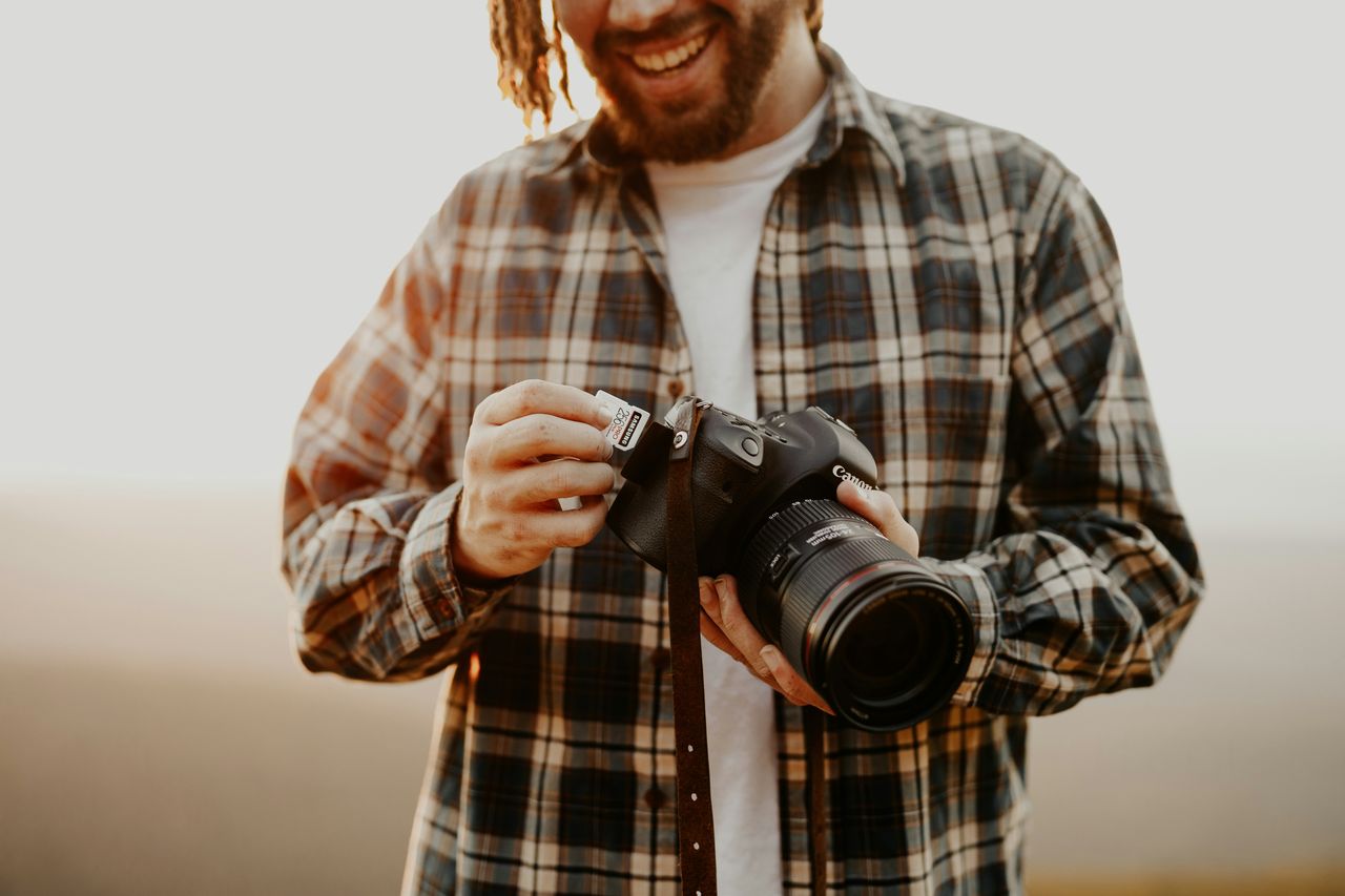 Fotógrafo sonriente insertando tarjeta de memoria SD en cámara Canon DSLR con lente profesional antes de una sesión, tarea habitual de preparación del asistente fotográfico